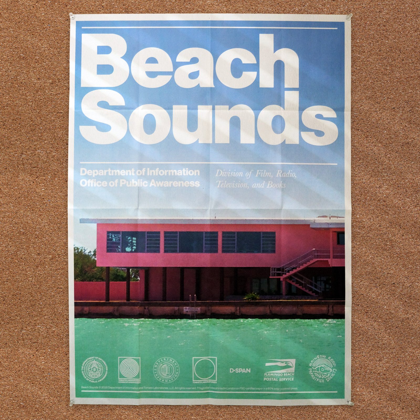 A vibrant and colorful newsprint poster of Beach Sounds is seen on a cork board