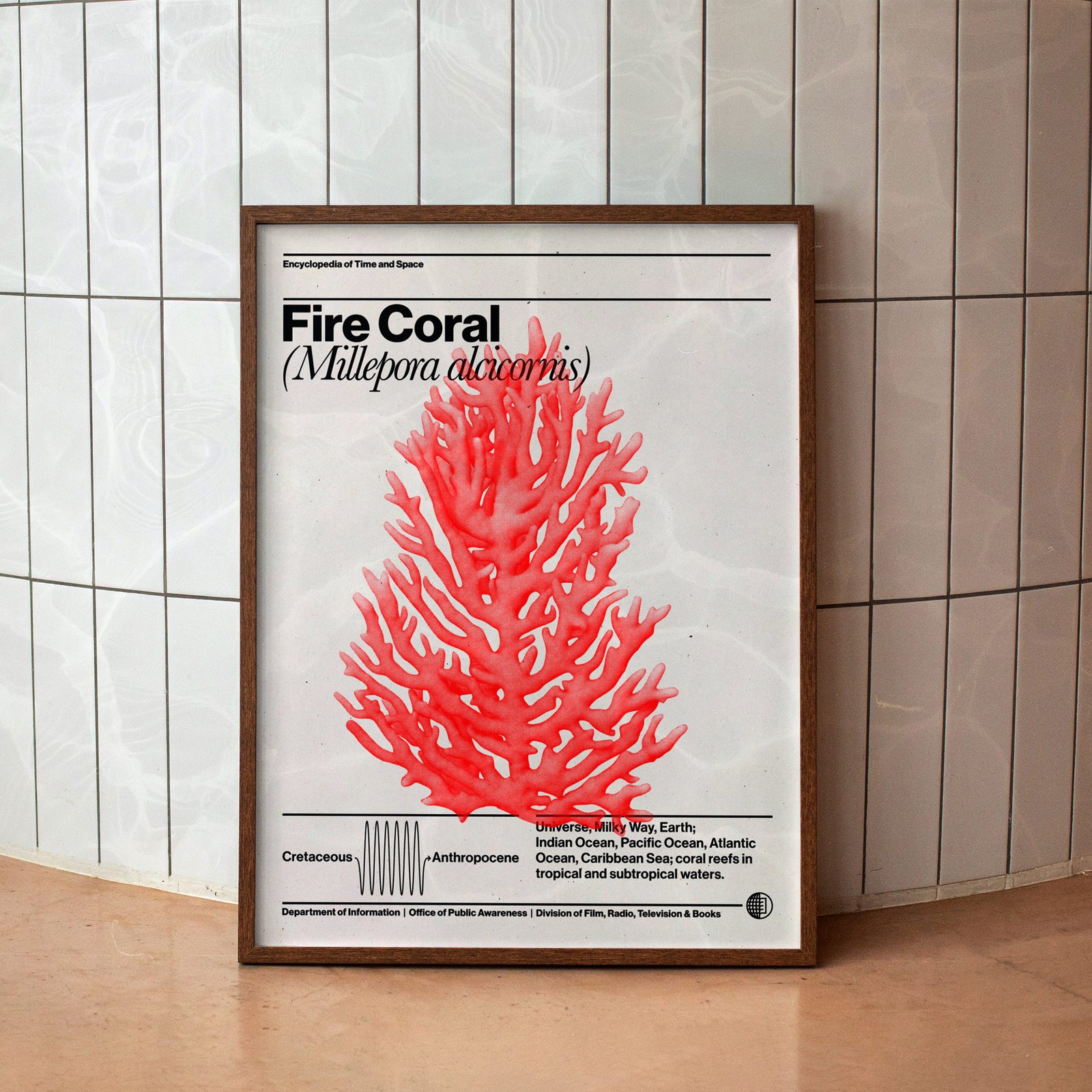 A framed poster of bright red fire coral over black text on white paper leans against a tiled wall inside an aquarium building with water texture reflections on it
