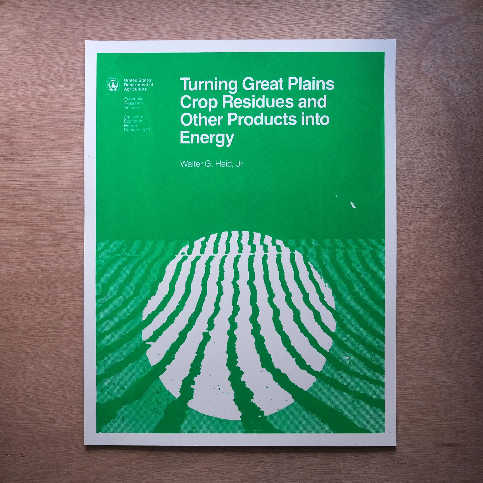 A bright green and white poster of the 1984 usda report cover for Turning Great Plains Crop Residues and Other Products into Energy sits on top of a wood surface