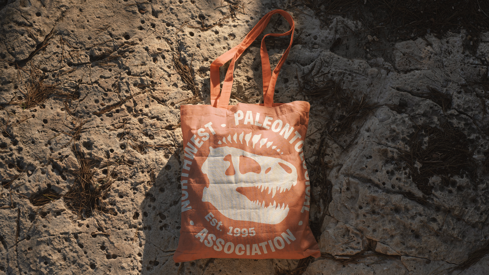 The Northwest Paleontological Association logo with a t-rex skull is seen on an orange tote bag
